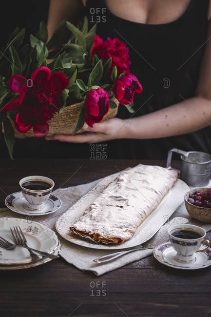 Woman holding flowers next to  sour cherries strudel dusted with powdered sugar