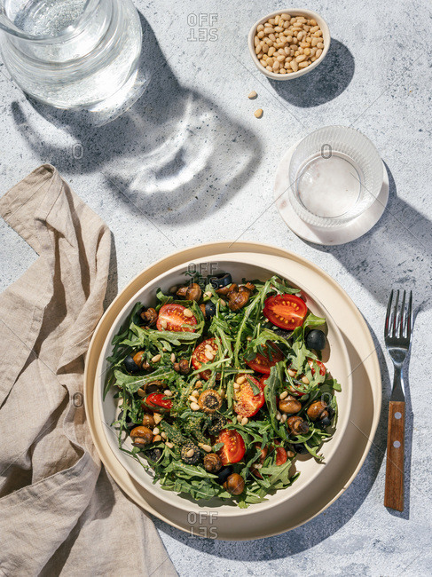 Salad with arugula, mini champignons, cherry tomatoes, black olives, pine nuts, nutritional yeast. Top view or flat lay. Copy space. Hard light. Vertical.