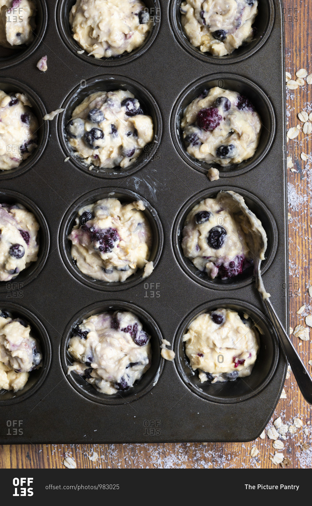 Mixed berry and oat muffin batter spooned into a patty cake pan.