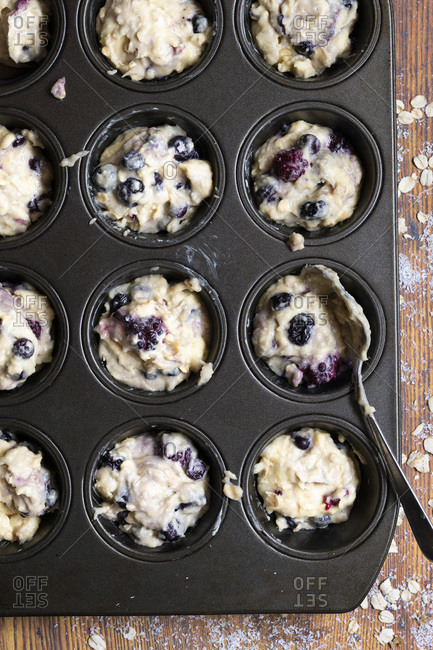 Mixed berry and oat muffin batter spooned into a patty cake pan.