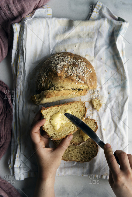 Woman spreading butter on a slice of homemade soda bread. Remaining slices accompany on a white cotton tea towel.