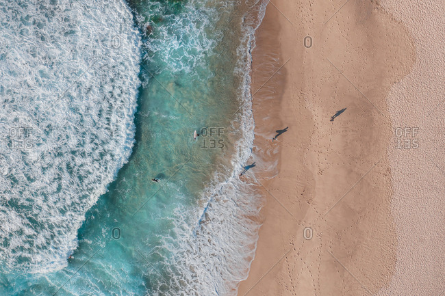 Aerial Top Down View Of Surfers Running From The Sand Into The Turquoise Ocean Waves At Bronte Beach In The Early Morning, Sydney, Australia