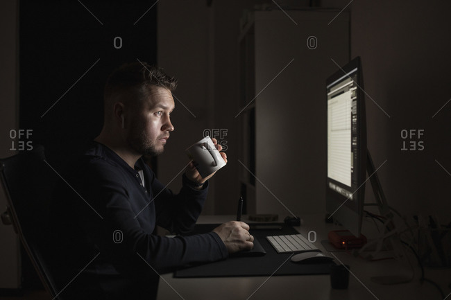 Man with coffee working late at computer in dark room