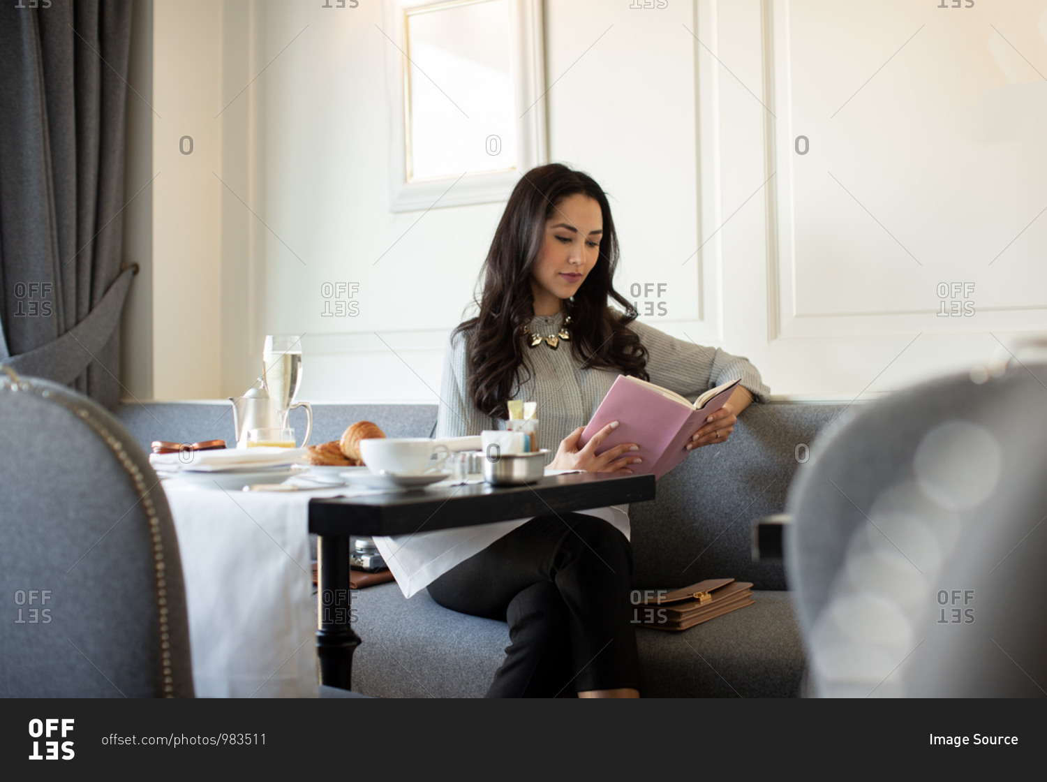 Young woman reading book while having champagne breakfast at boutique hotel in Italy