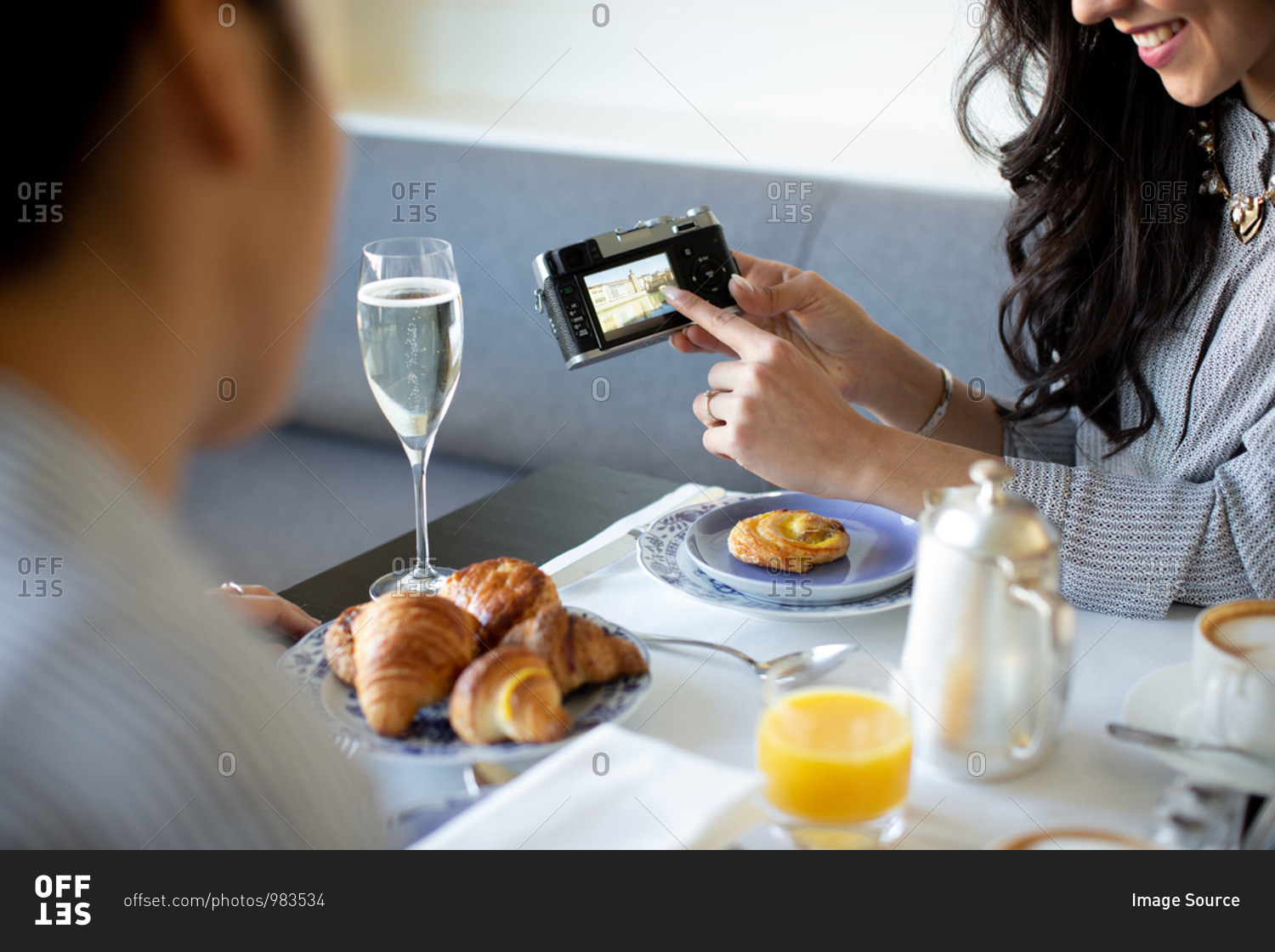 Young woman pointing at digital camera while having champagne breakfast at boutique hotel in Italy