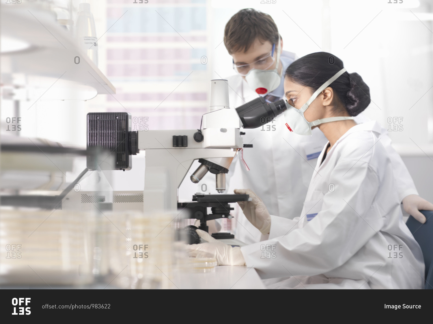 Scientists in isolation environment wearing masks, working in research laboratory, using microscope.