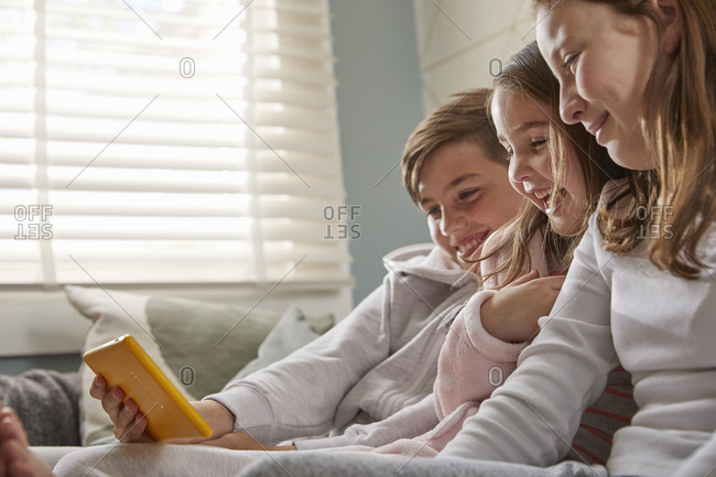 Group of children sitting on a sofa in their pajamas, looking at digital tablet.