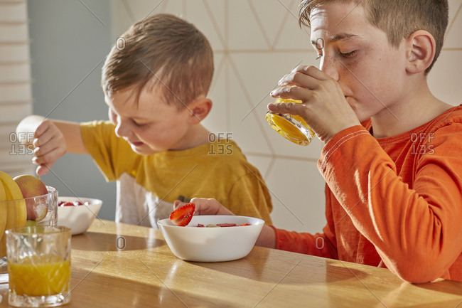 Two boys sitting at kitchen table, eating breakfast.