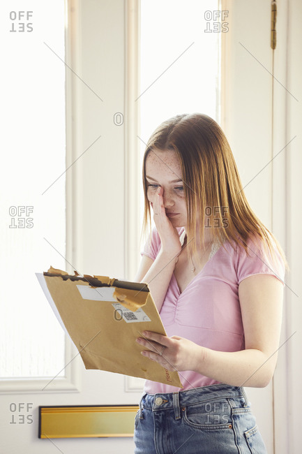 Teenage girl standing in hallway holding large envelope with letter.