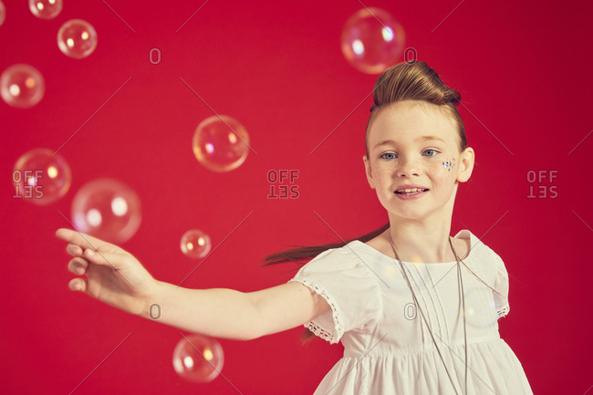 Portrait of brunette girl wearing romantic white dress on red background, surrounded by soap bubbles.