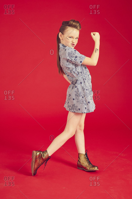 Portrait of brunette girl wearing blue dress and combat boots on red background.