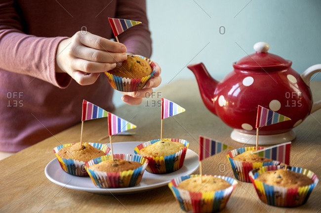 High angle view of red tea pot and decorated cupcakes on a kitchen table.