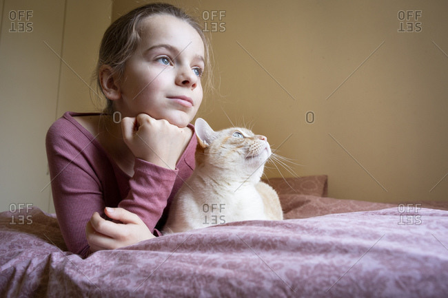 Portrait of girl and white and ginger cat lying on bed.