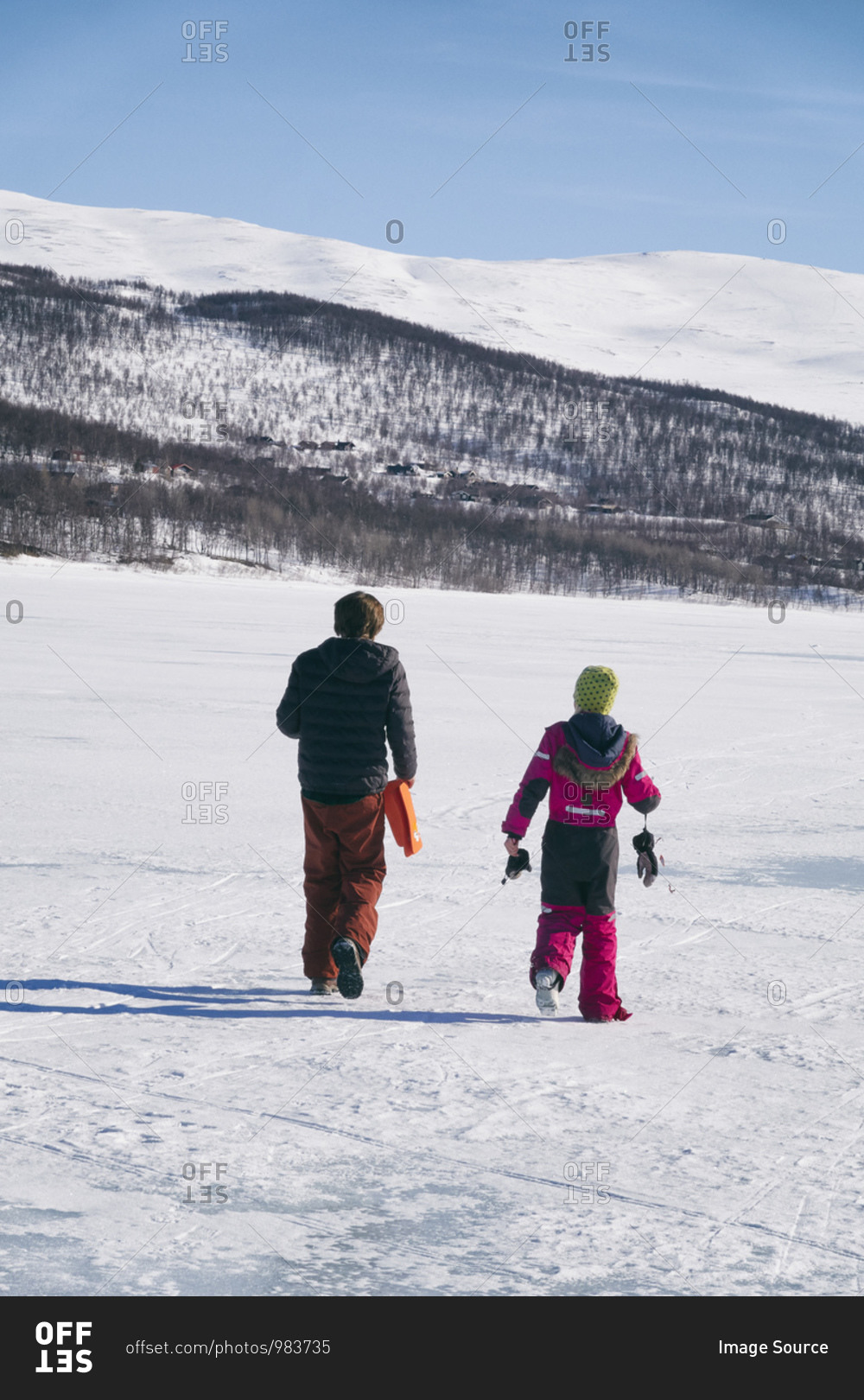 Rear view of two boys walking on frozen lake in Vasterbottens Lan, Sweden.