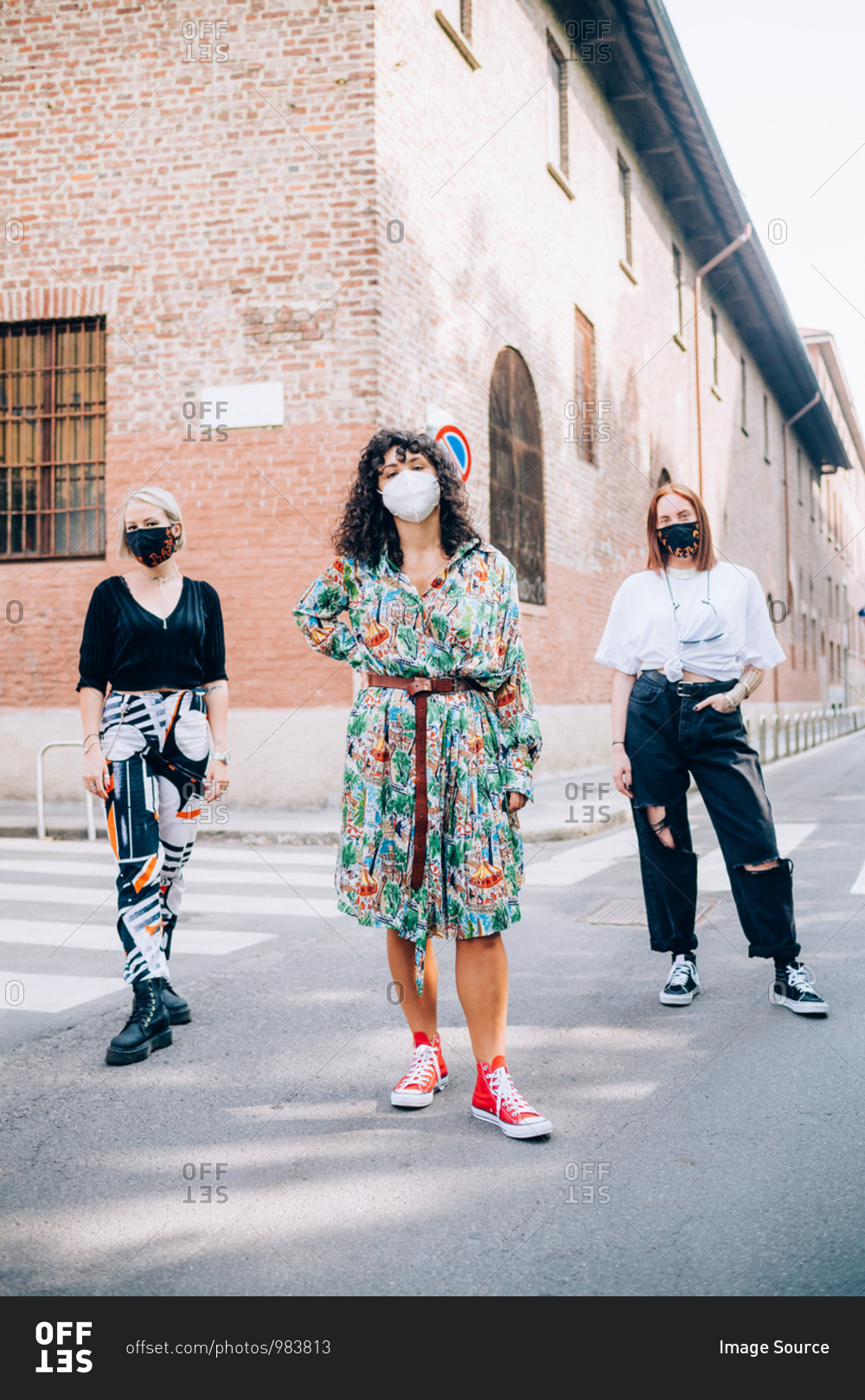 Three young women wearing face masks during Corona virus, standing on a pedestrian crossing in a street.