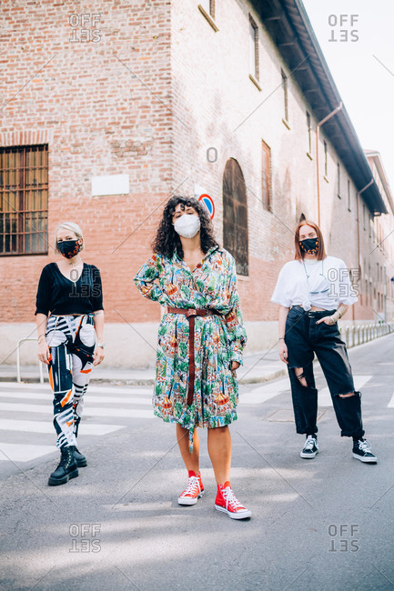 Three young women wearing face masks during Corona virus, standing on a pedestrian crossing in a street.