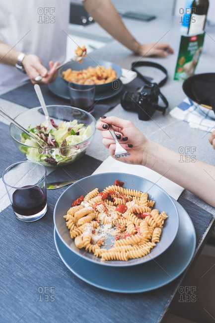 High angle close up of two people standing at a table, eating bowls of Fusili pasta.