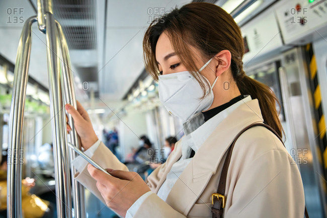 Young woman wearing a mask checking her phone on the train