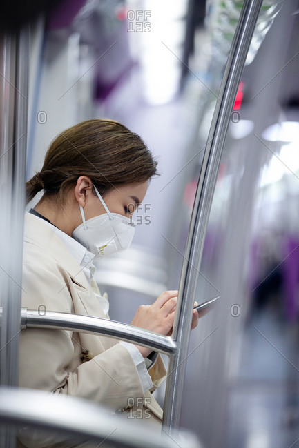 Young woman wearing a mask checking her phone on the subway