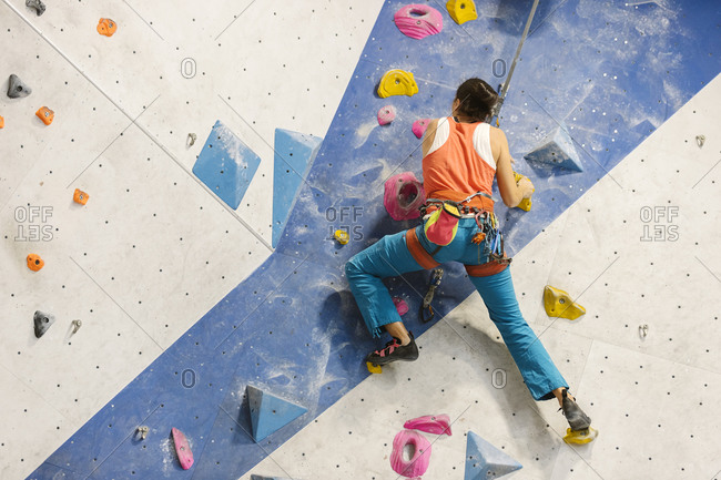 Adult woman wearing an orange tank top and blue pants climbing on indoor rock wall