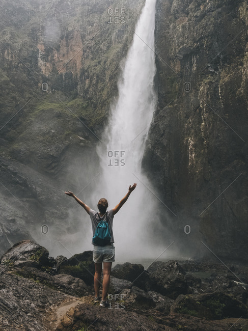 Rearview of a young woman opening arms while looking at the waterfall, Queensland, Australia.