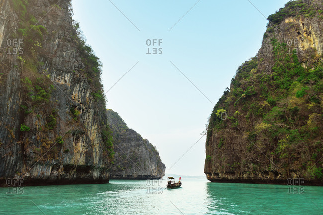 Landscape of a ship sailing between two rocks with vegetation.