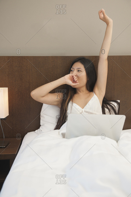 Beautiful woman waking up and checking her laptop in hotel room
