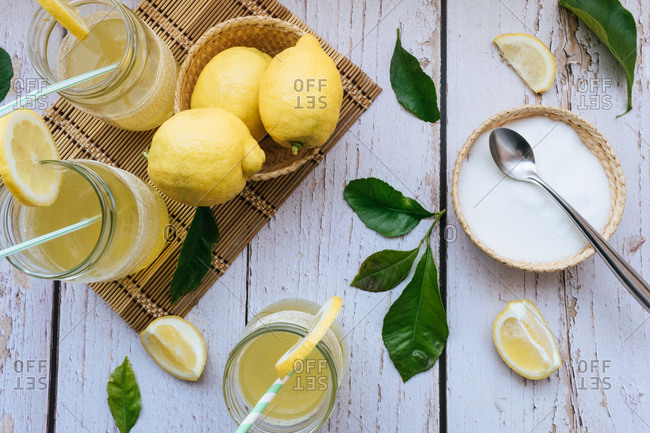 Top view of glasses of lemonade with lemons and sugar on a white table