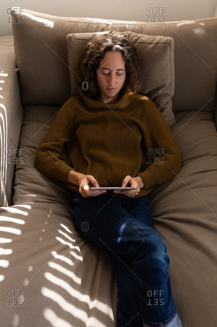 A Caucasian woman spending time at home, using her tablet, resting on couch. Lifestyle at home isolating, social distancing in quarantine lockdown during coronavirus covid 19 pandemic.