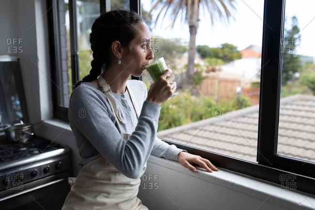 A Caucasian woman spending time at home, drinking smoothie. Lifestyle at home isolating, social distancing in quarantine lockdown during coronavirus covid 19 pandemic.