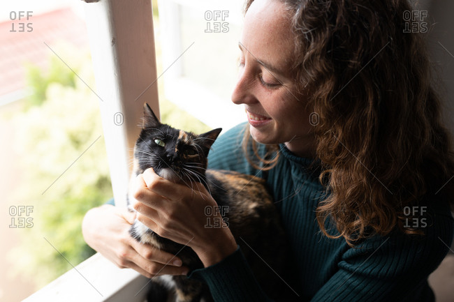 A Caucasian woman spending time at home, petting her cat. Lifestyle at home isolating, social distancing in quarantine lockdown during coronavirus covid 19 pandemic.