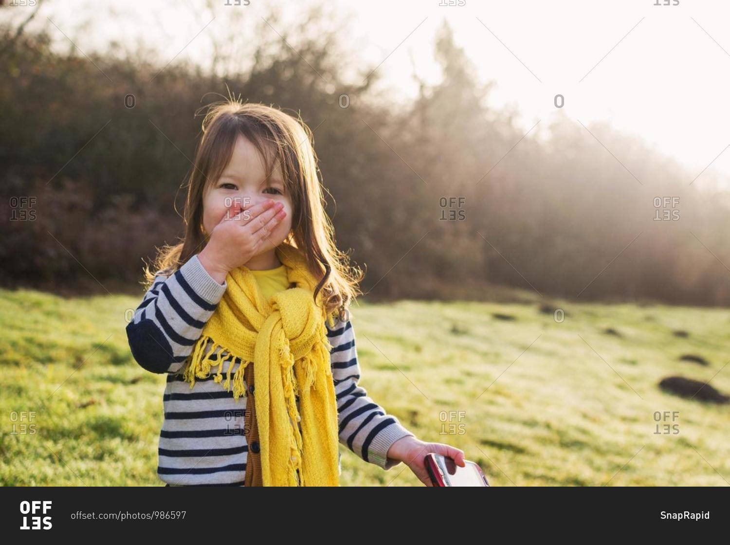 Laughing girl with hand in front of her mouth, holding mobile phone