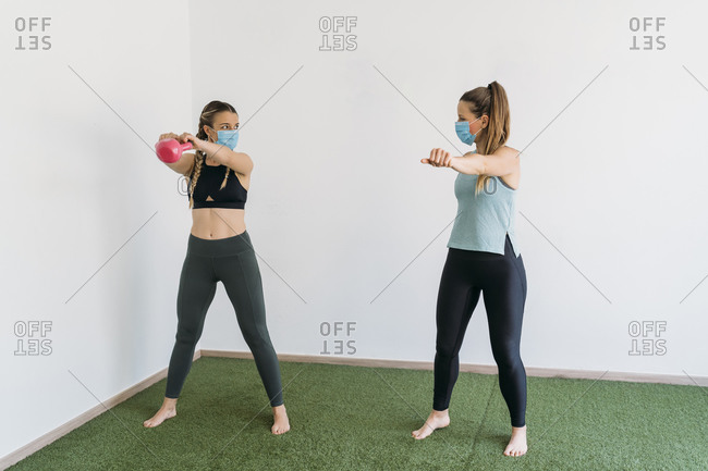 Woman wearing face mask exercising with coach at health club