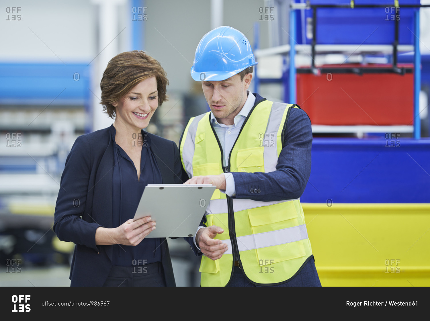 Supervisor explaining plan to happy female manager on clipboard in factory