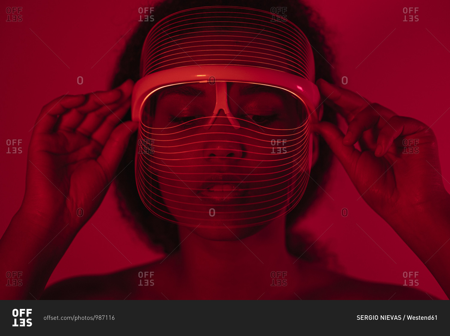 Close-up of young woman wearing red led mask against wall at home