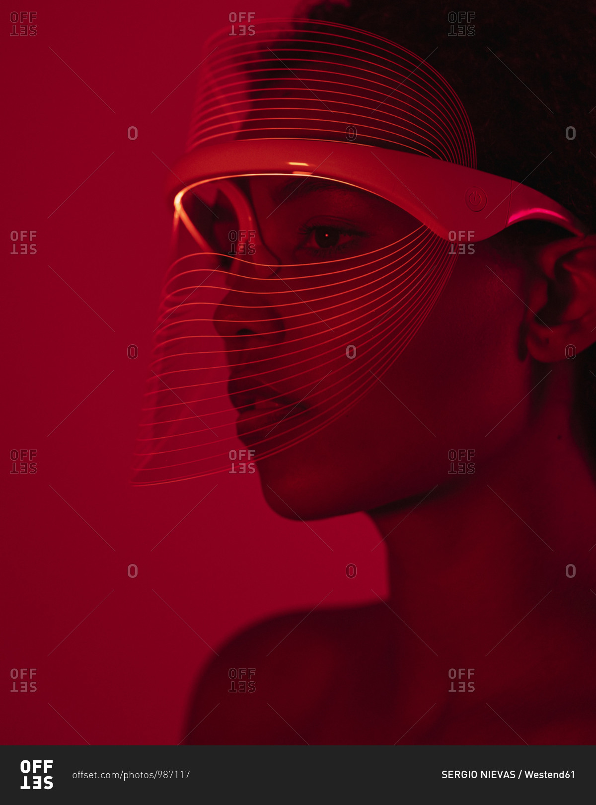 Close-up of woman wearing red light therapy mask against wall at home