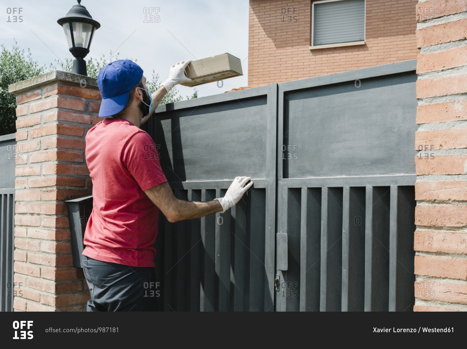Male delivery person giving package from over gate of house