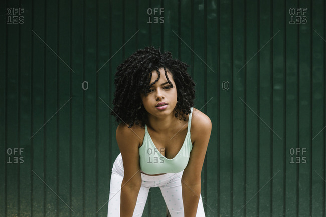 Beautiful young woman bending over against green metal door