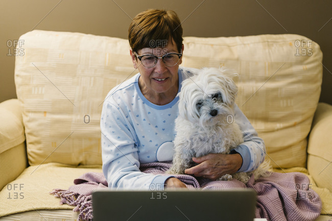 Ill senior woman sitting with dog while discussing over video call through laptop at home