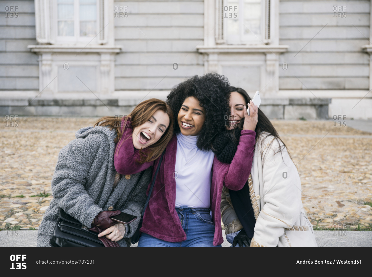 Happy young woman embracing female friends while sitting against Madrid Royal Palace- Spain