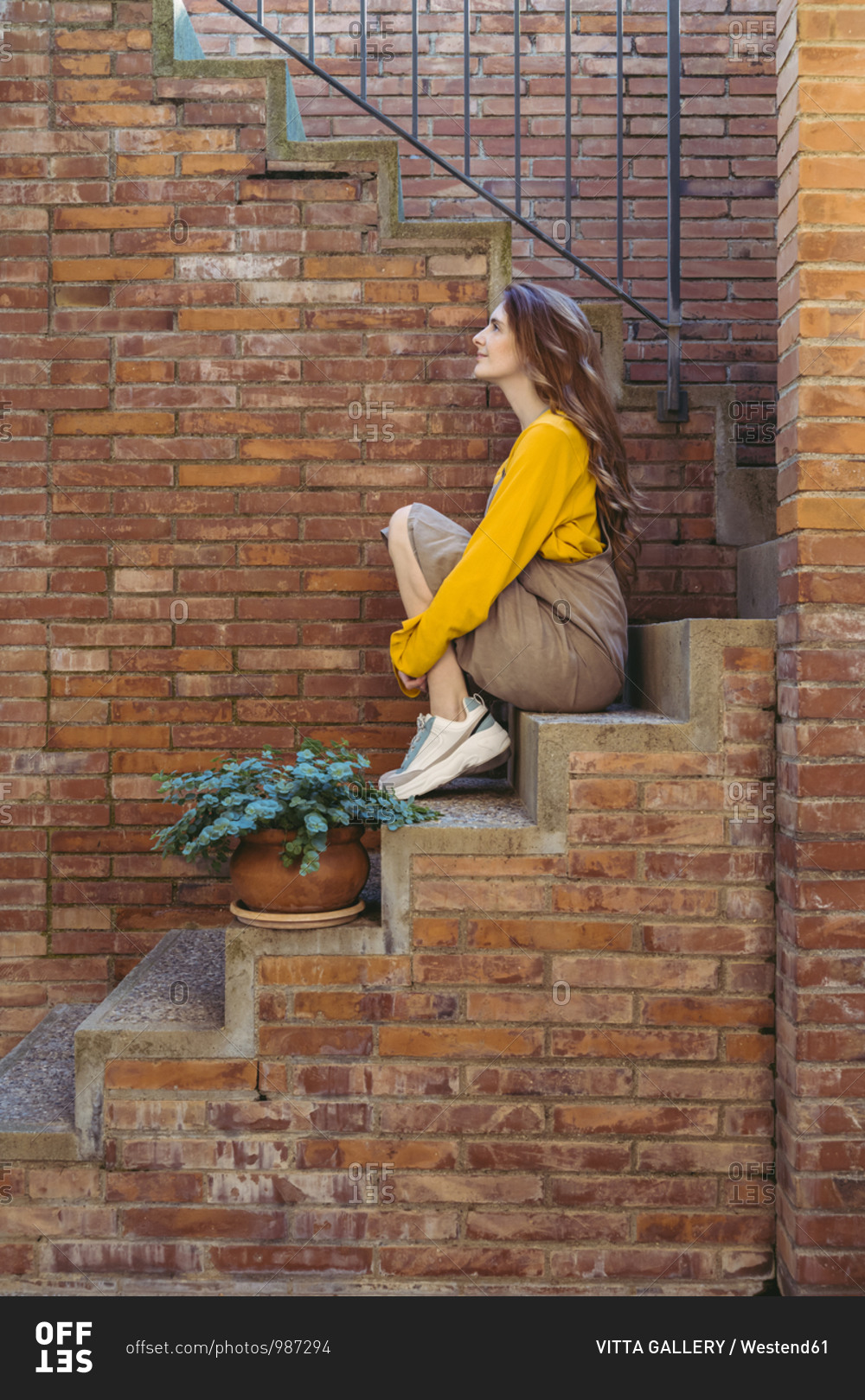 Thoughtful young woman hugging knees while sitting on staircase