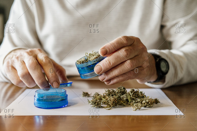 Midsection of senior man grinding weed in grinder at home