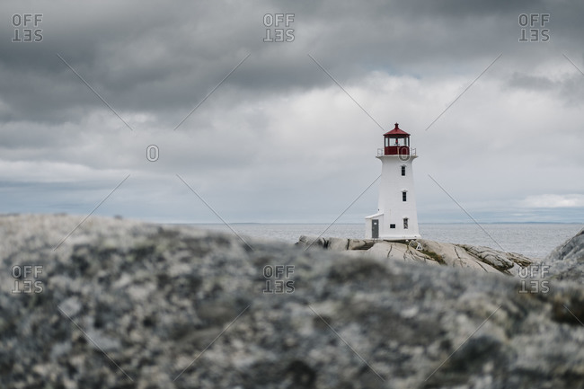 Peggys Point Lighthouse on rock formation by sea against cloudy sky- Nova Scotia- Canada