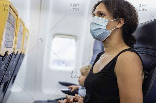 Mother and son waiting for flight departure in airplane wearing masks during pandemic