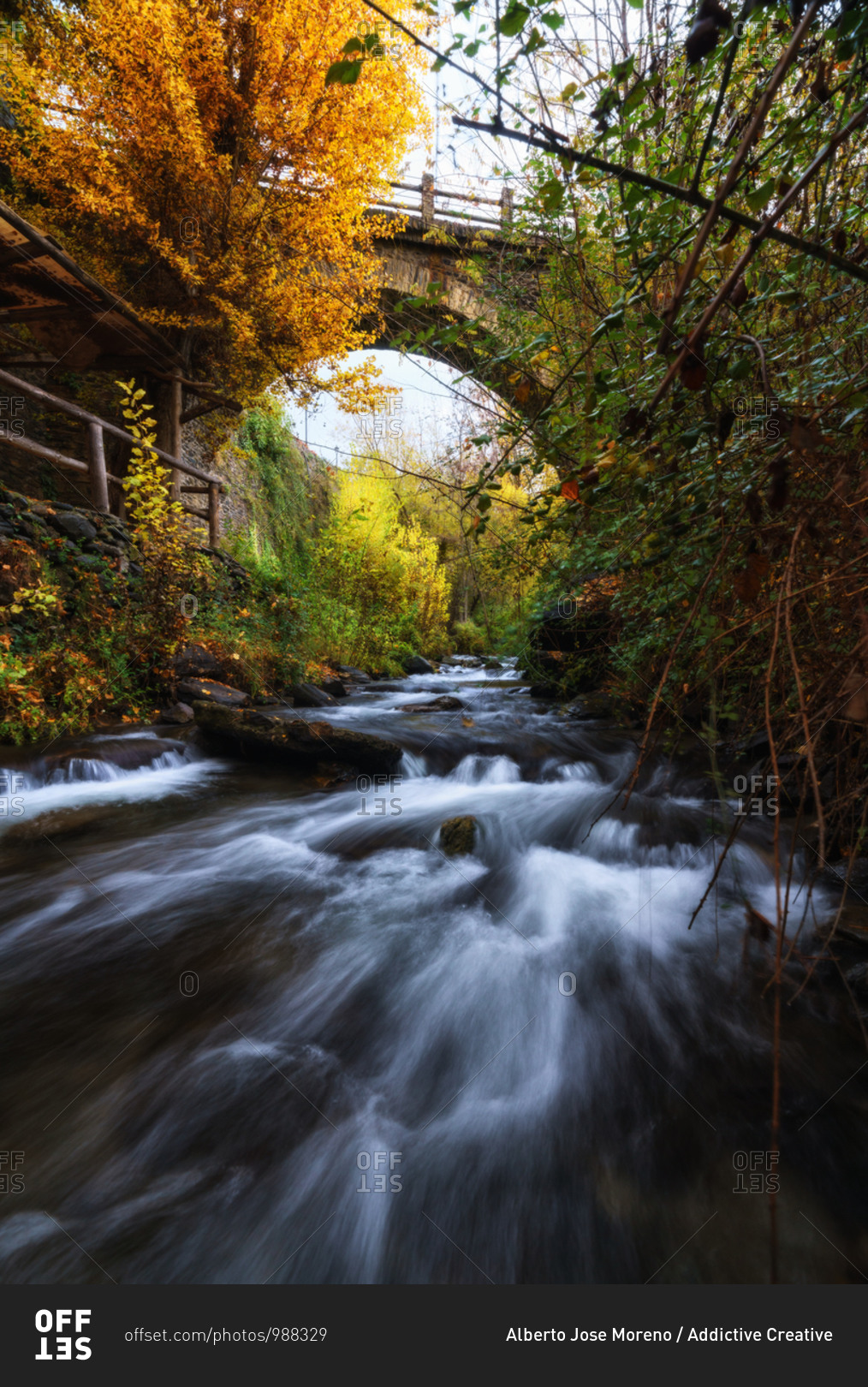 Majestic scenery of river flowing through forest and under bridge in long exposure in Granada