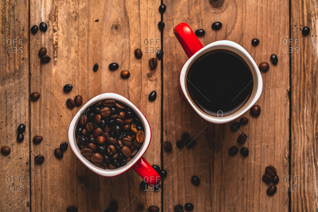 Top view composition of red cups with roasted aromatic coffee beans and fresh hot energizing americano placed together on wooden table