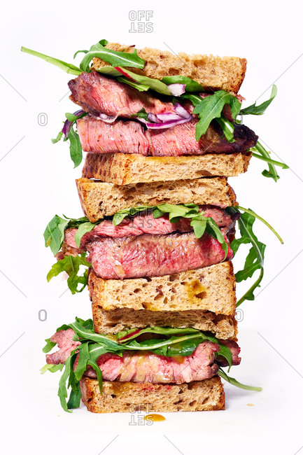 Close up of a pile of beef steak sandwich with arugula and mustard dressing against bright background