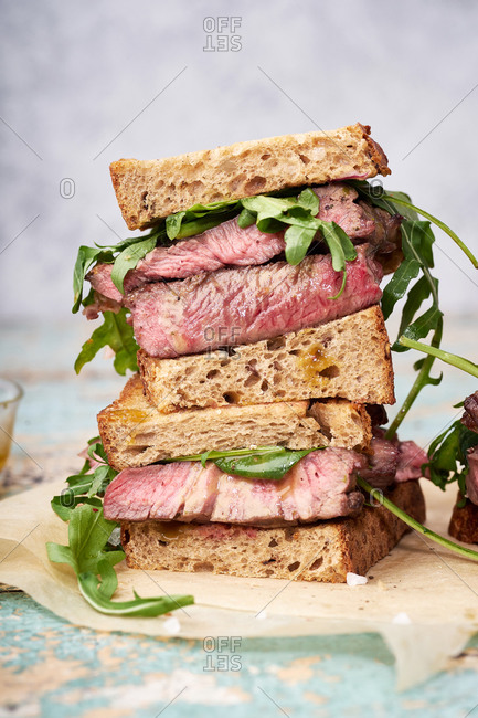 Close up of a pile of beef steak sandwich with arugula and mustard dressing against bright background