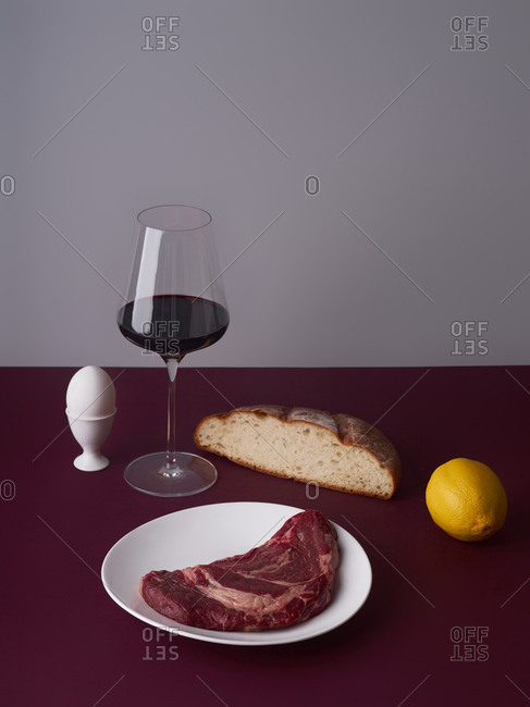 Still life with a glass of wine, beef steak and bread slice.