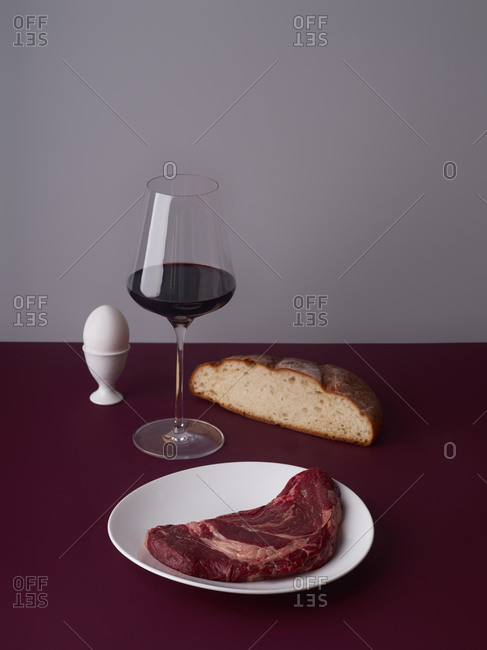 Still life with a glass of wine, beef steak and bread slice.